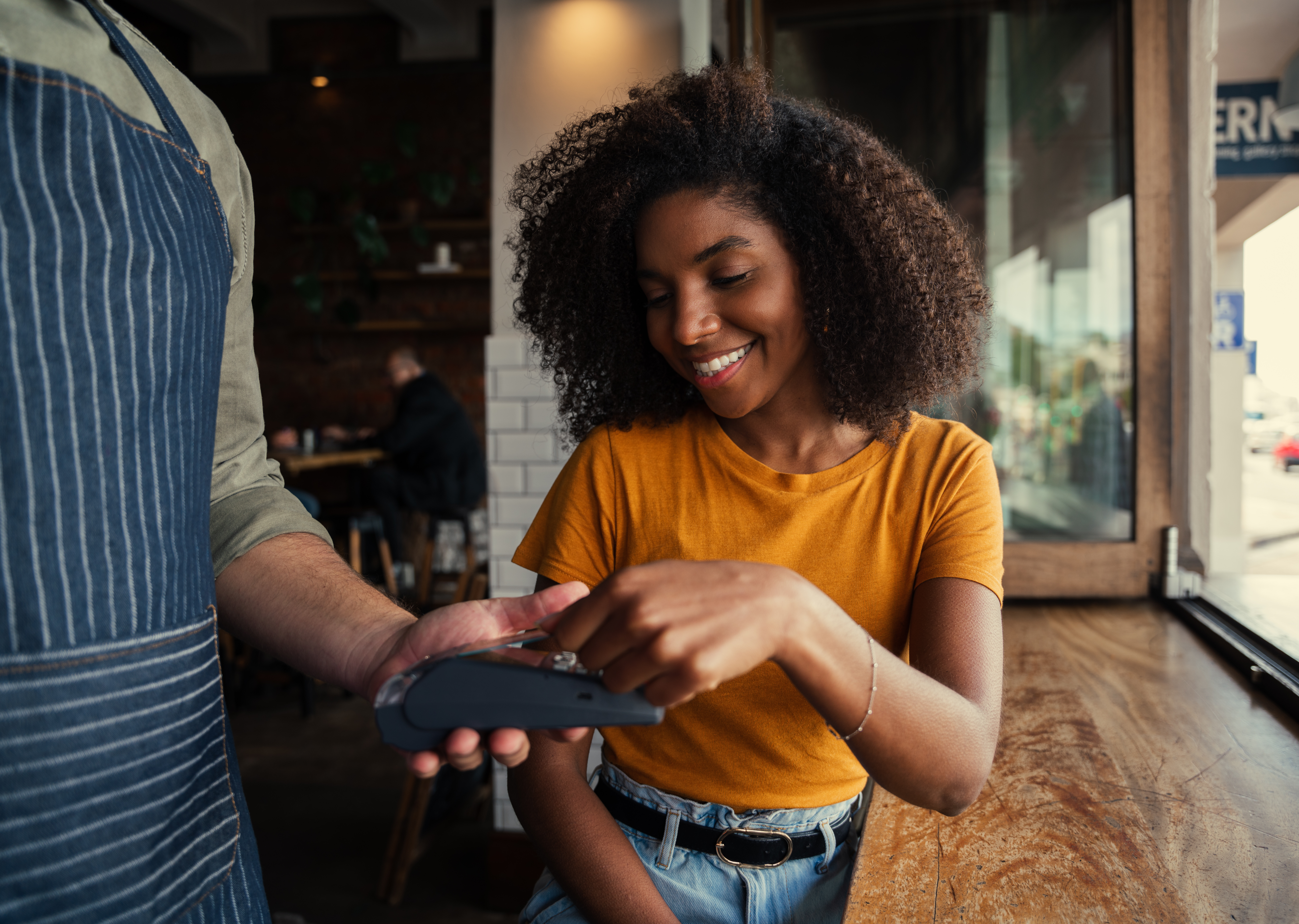 A young black female taps her debit card against a card reader while at a cafe.