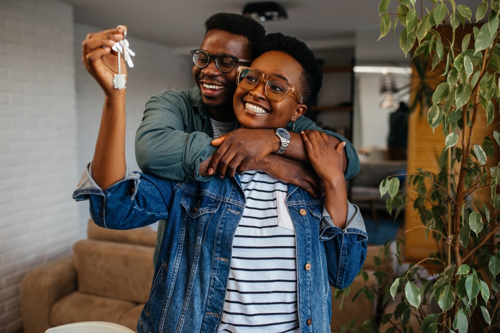 A young couple embrace. The female holds house keys in her hand.