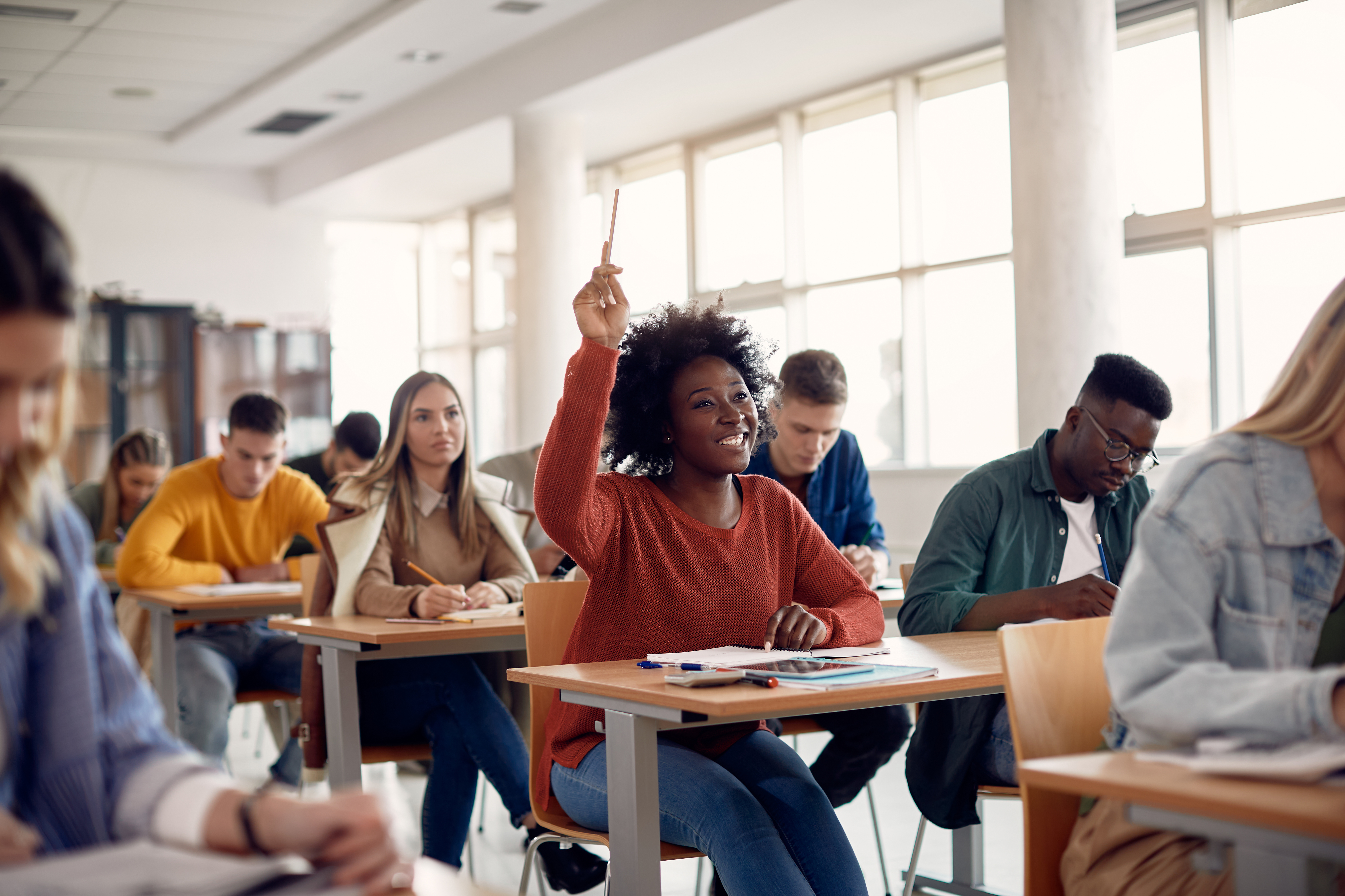 Student raising arm to answer question while attending class with her university colleagues.