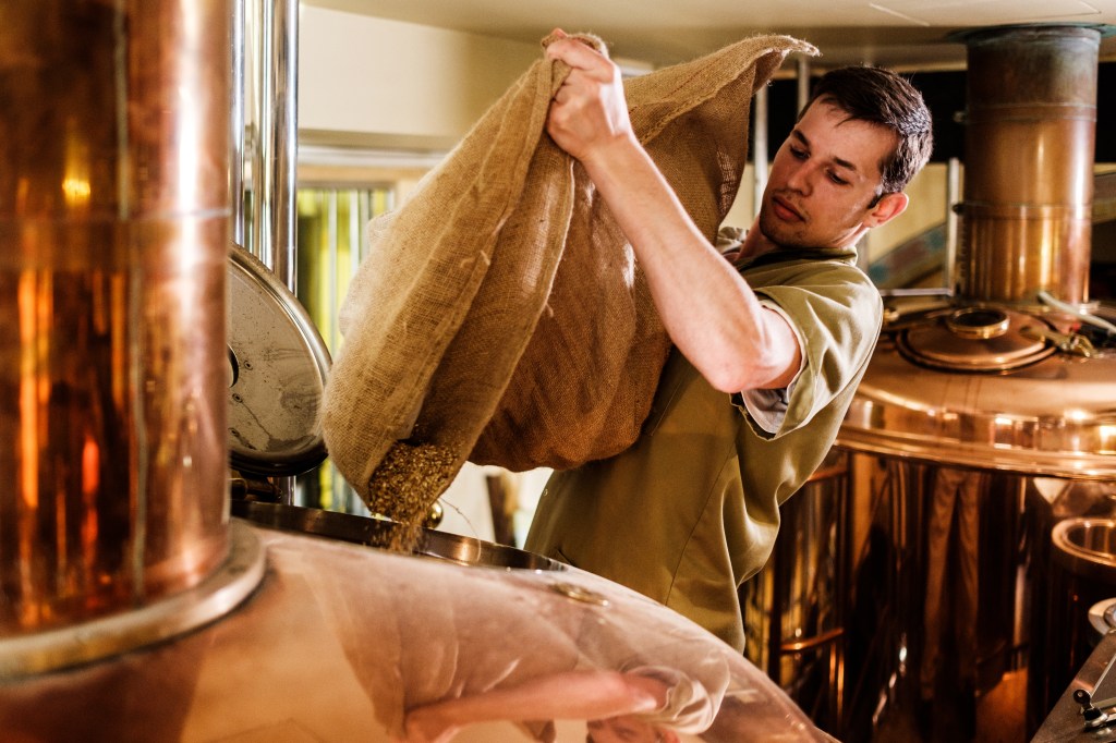 An employee pours a bag of coffee beans into a large roaster.