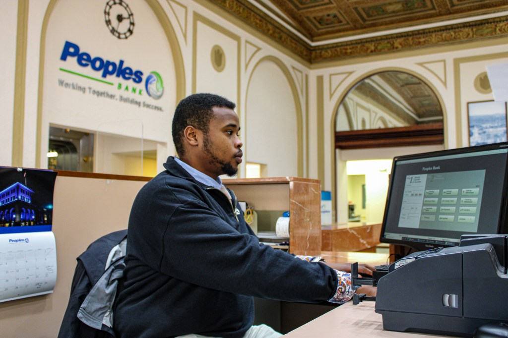 A Peoples Bank employee makes a transaction for a customer who stands in the teller line.