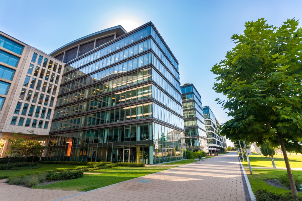 A large, glass business complex with a brick sidewalk.