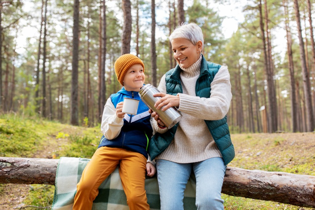 Grandmother with grandson drinking hot chocolate in the woods during a cold day.