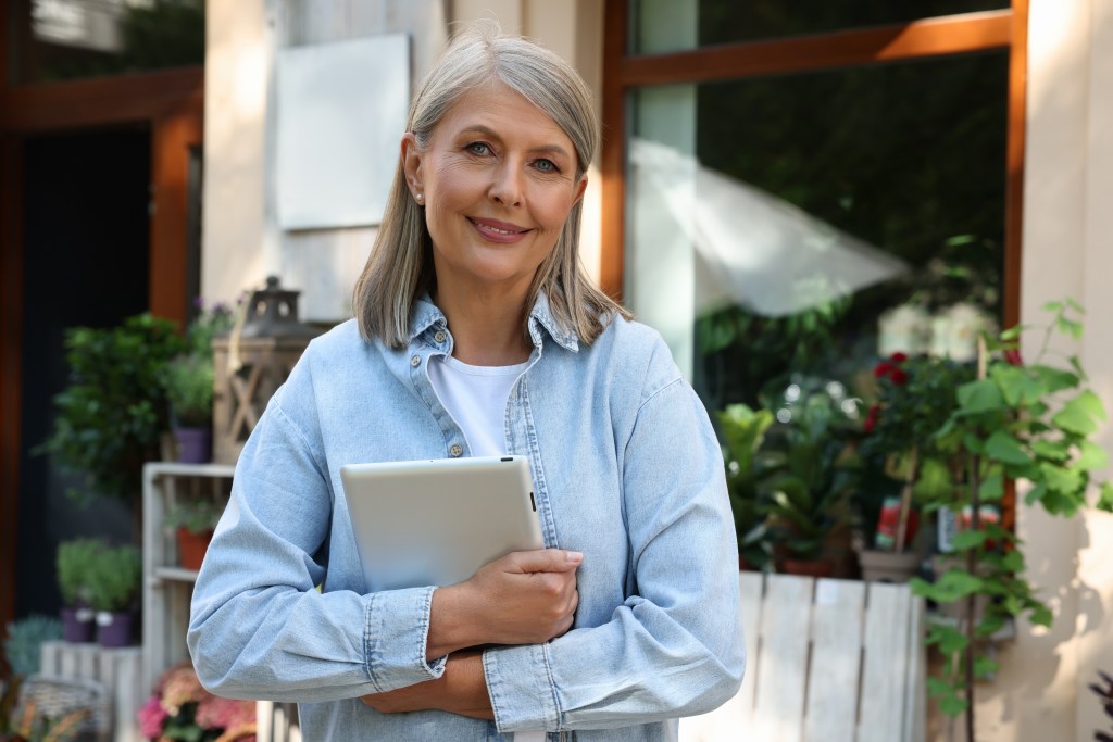 Smiling business owner with tablet near her flower shop outdoors.
