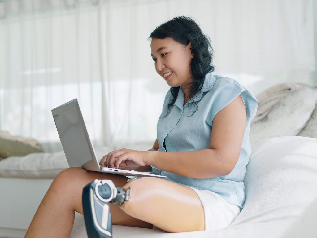 Happy adult woman with prosthetic leg typing on laptop.