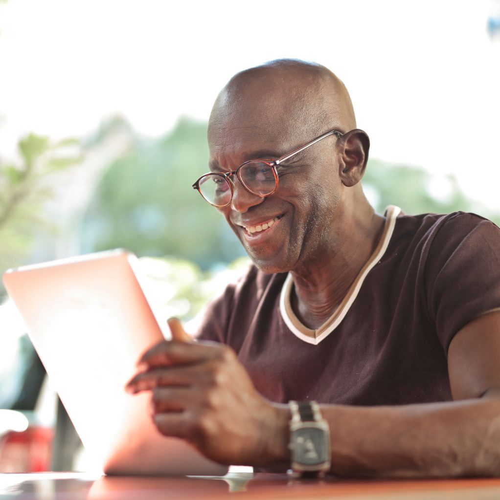 Mature man looks at at a tablet while sitting in an outdoor cafe.