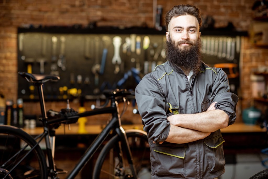 Bearded repairman in workwear at a bicycle workshop.