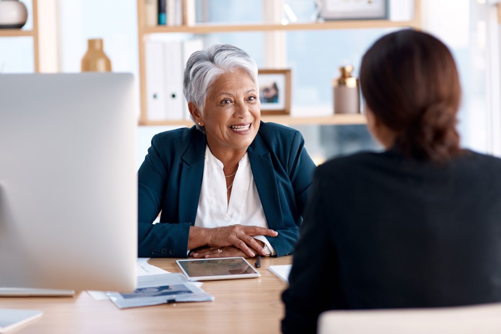 An HR representative sits down at an office desk with a co-worker.