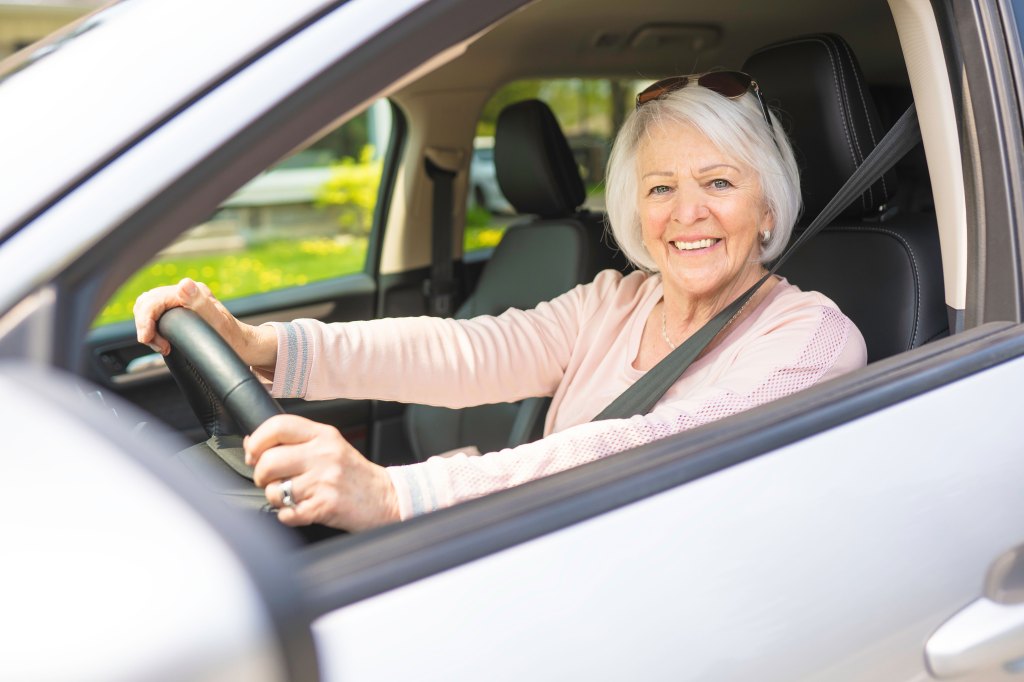 Happy and smiling senior woman driving a silver sedan.