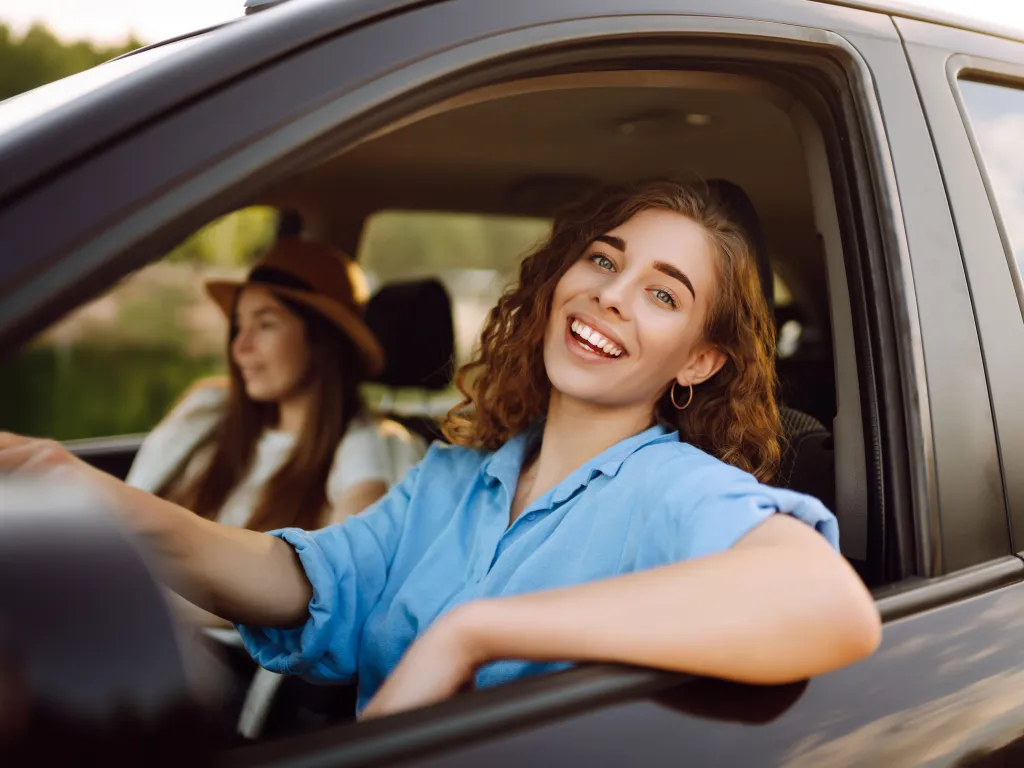 A female and her daughter sing along to music as they drive in a car through town.