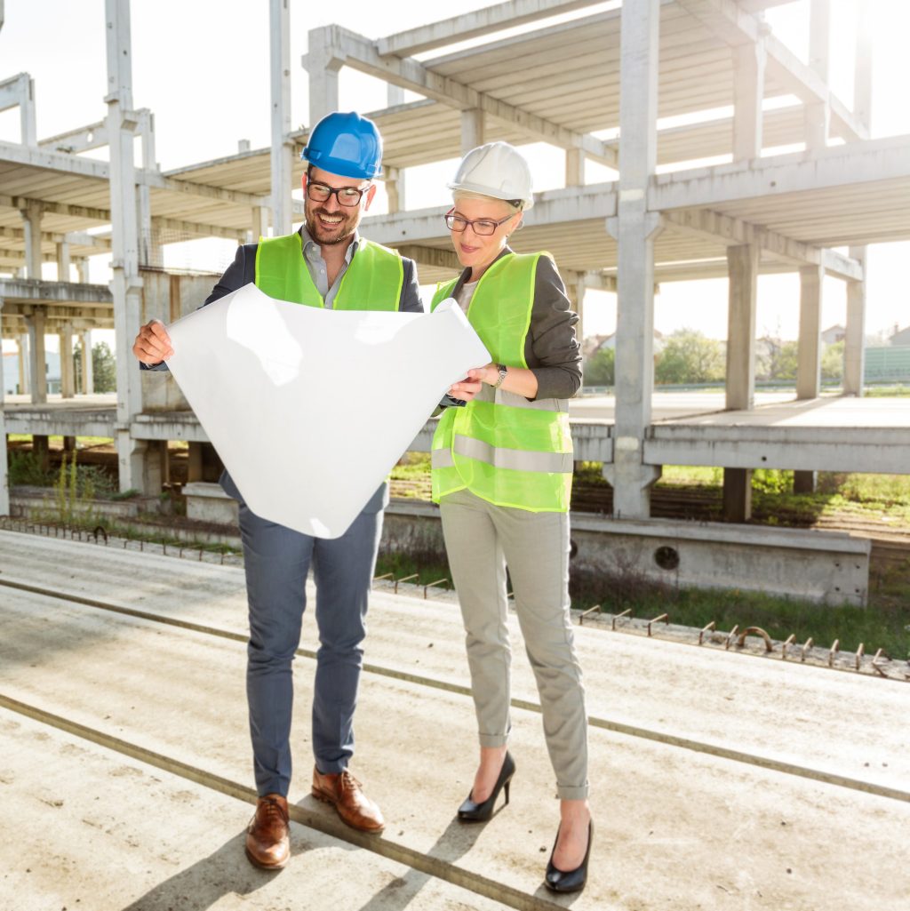 Young female and male business partners at construction site, discussing and planning. One person talking on the phone, blurred in background.