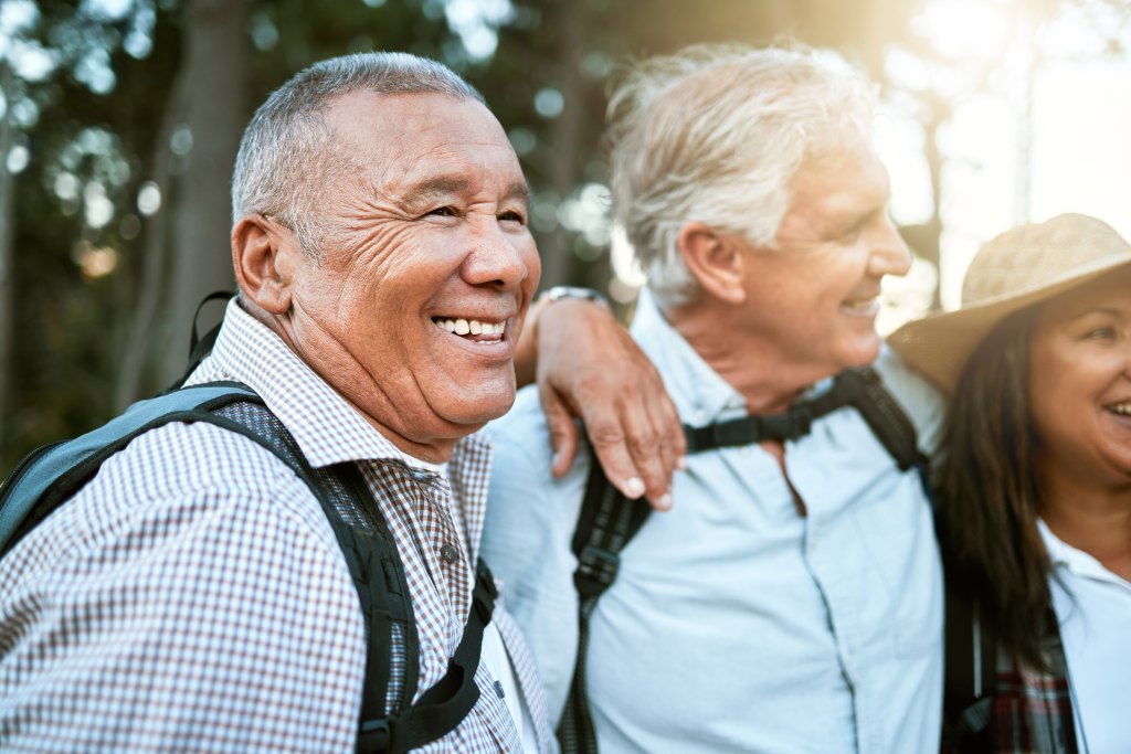 Senior male wearing backpack with his friend enjoying a walk in the forest.