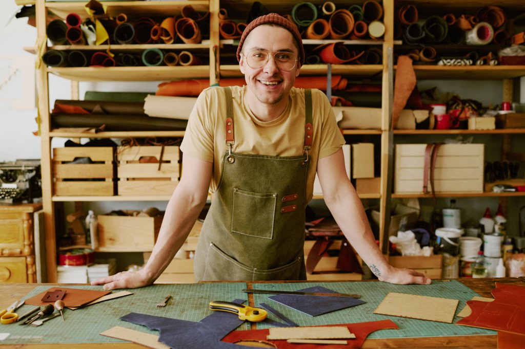 Young male tailor leaning on antique wooden table. 
