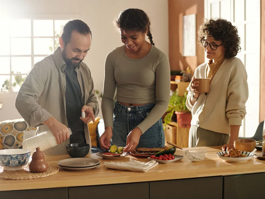 Parents with daughter preparing sandwiches together standing in kitchen.