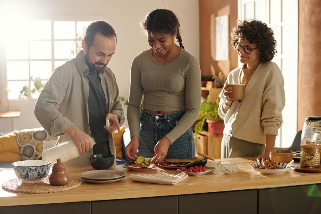 Parents with daughter preparing sandwiches together standing in kitchen.
