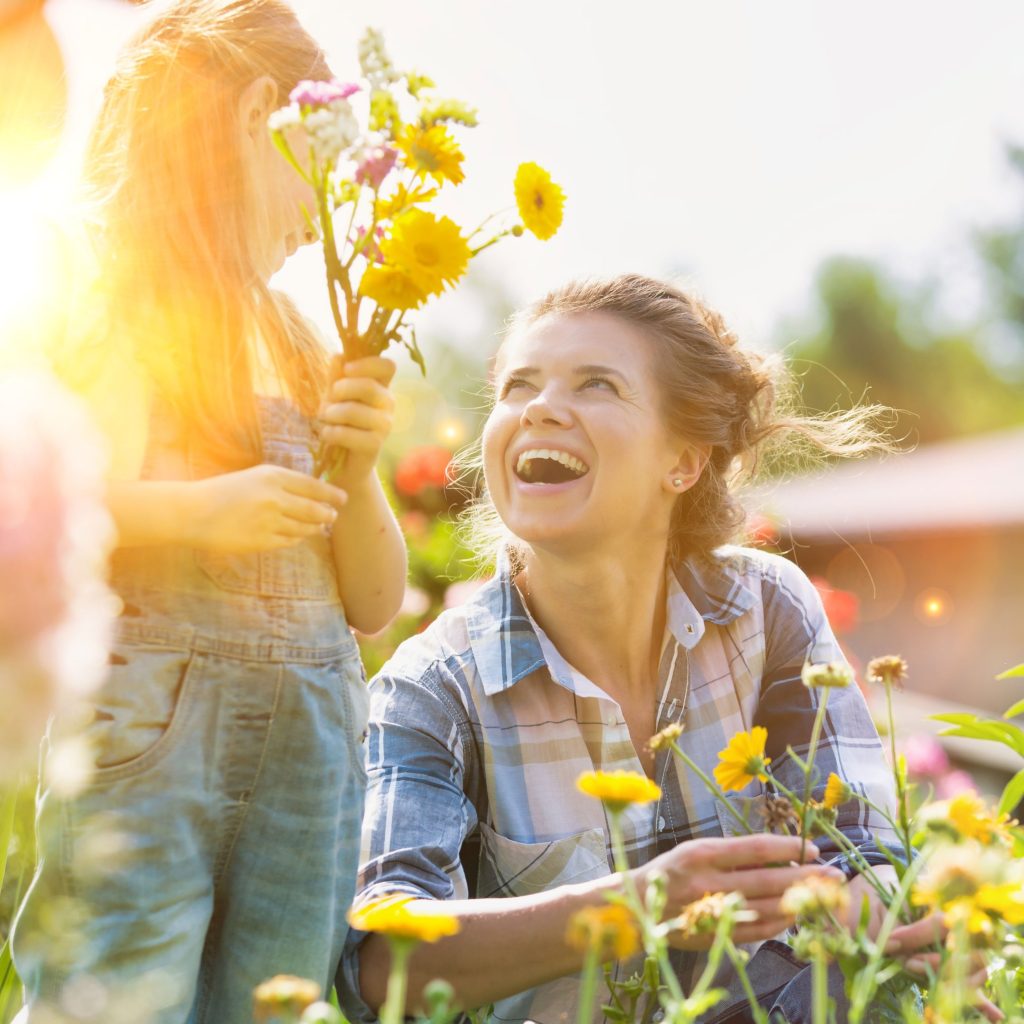 Mother and daughter picking pretty colourful flowers in their organic garden with yellow lens flare in background.