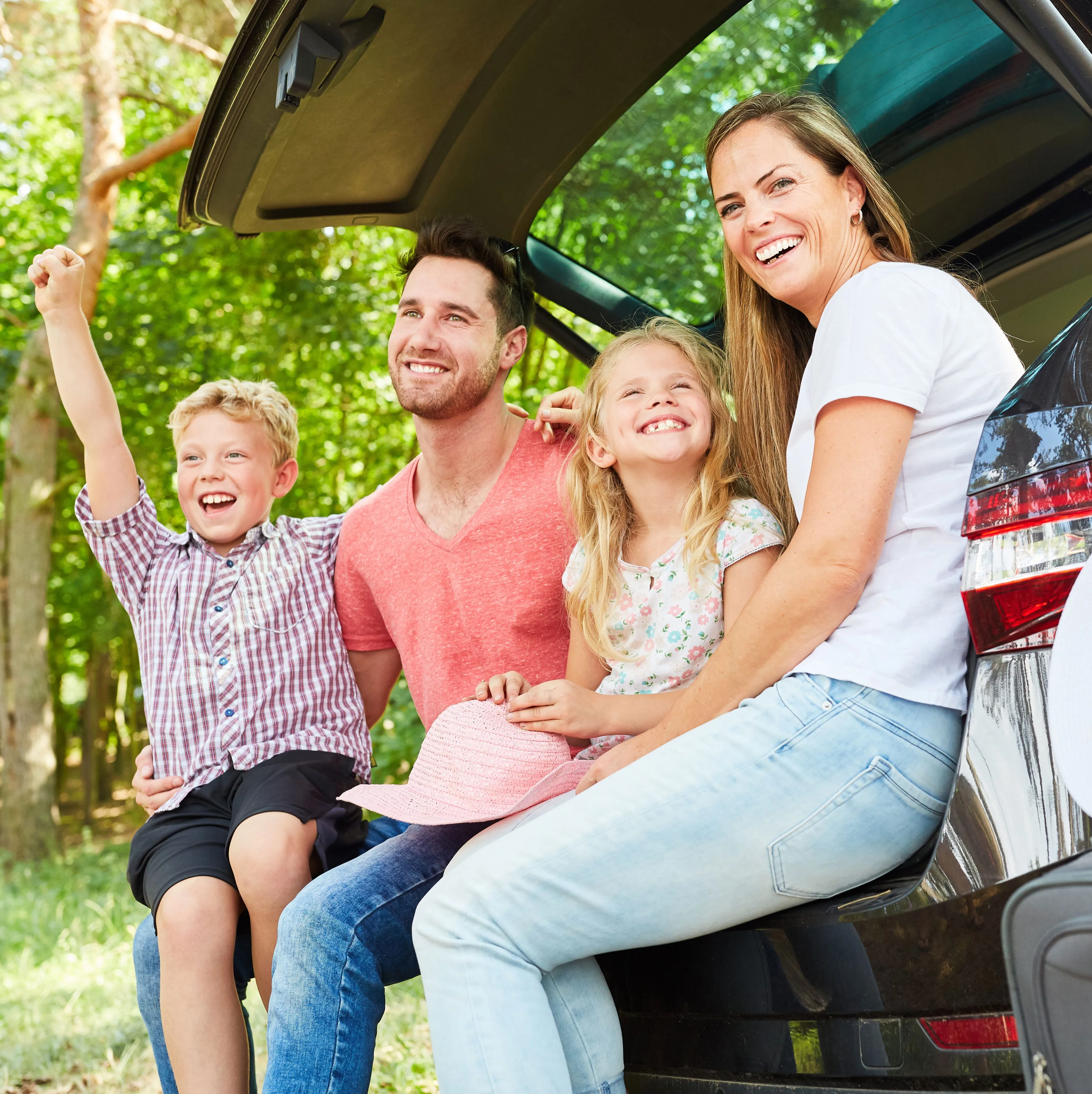 Two parents and two children sit in the hatch of their car while packing for vacation.