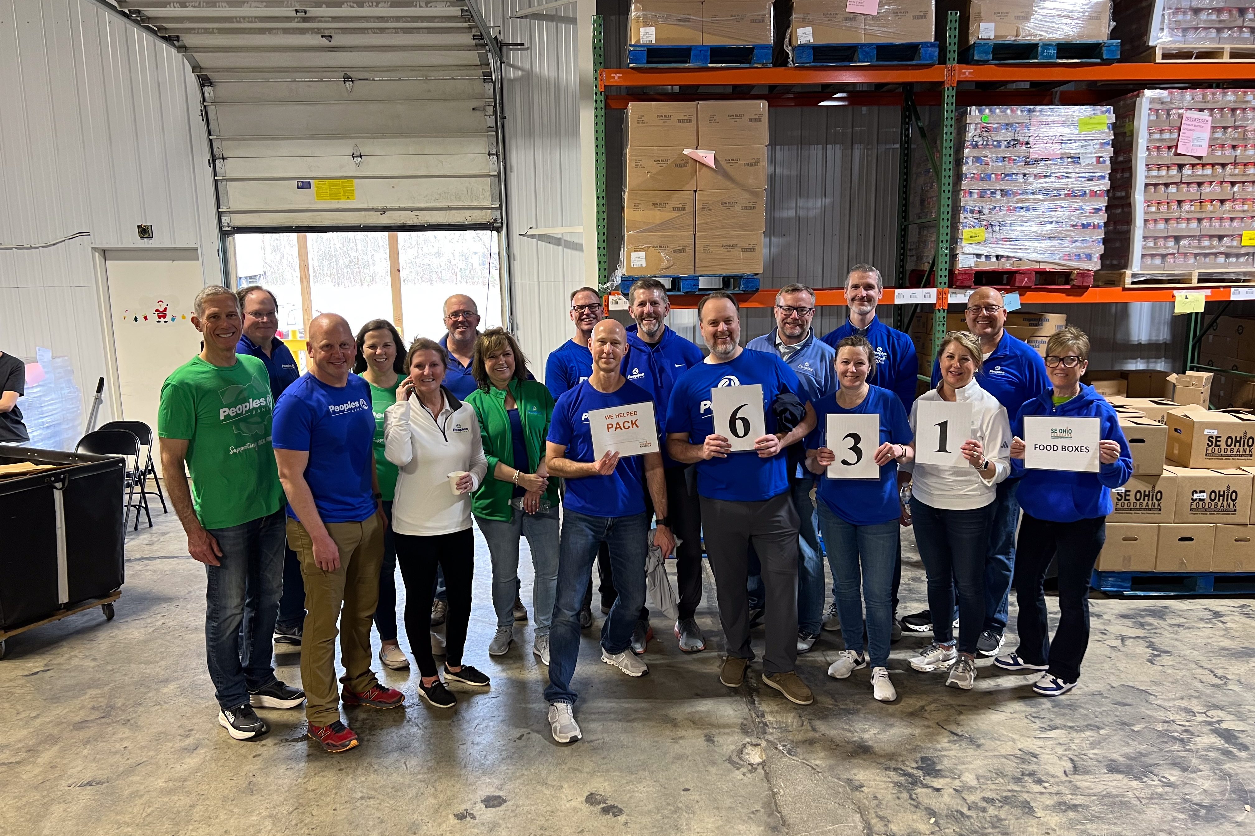Peoples Bank executives stand in the SE Food Pantry holding signs marking 631 donation boxes filled.