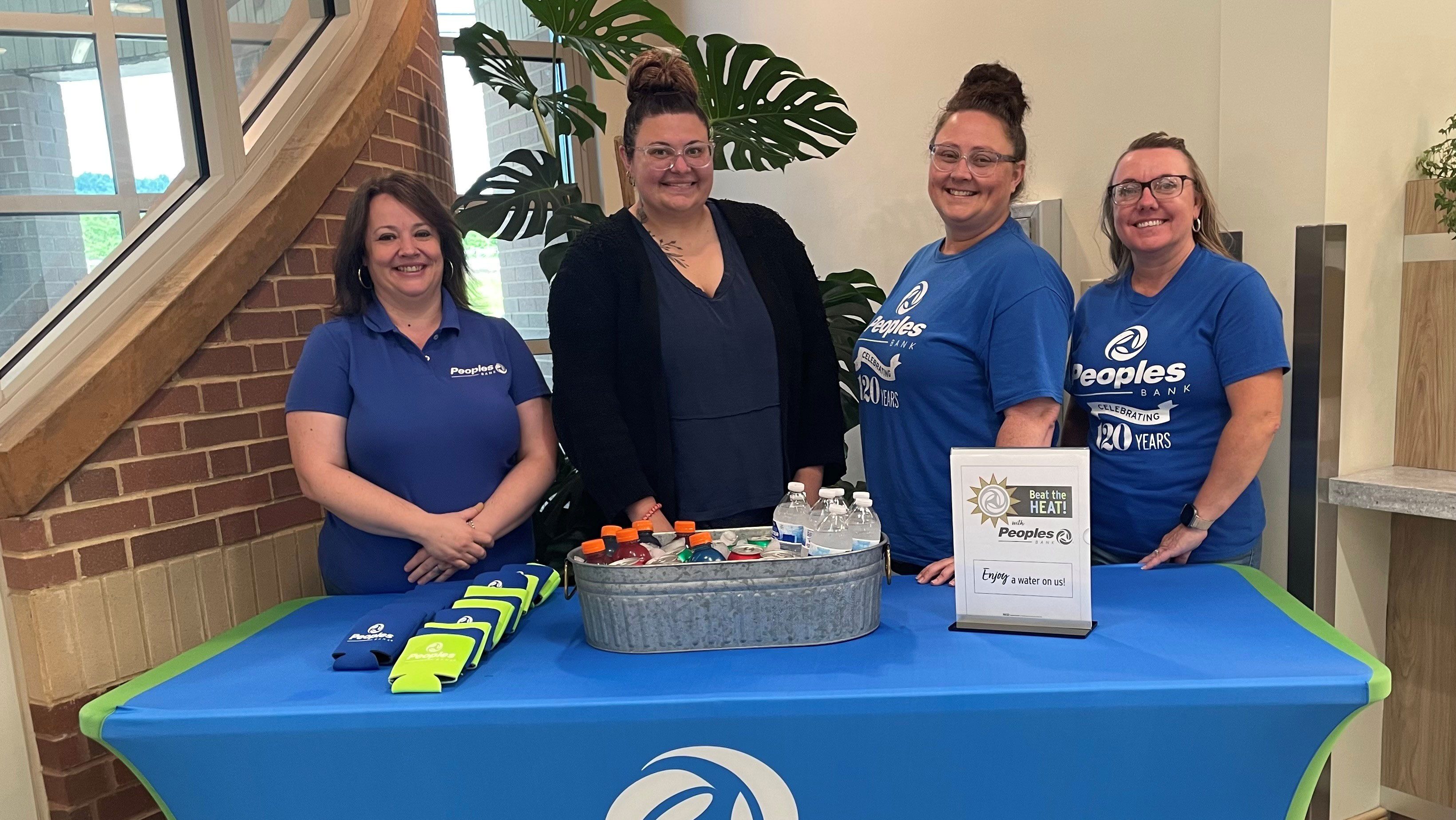 Four Peoples Bank associates stand behind a table filled with koozies, water, sports drinks and soda pop.