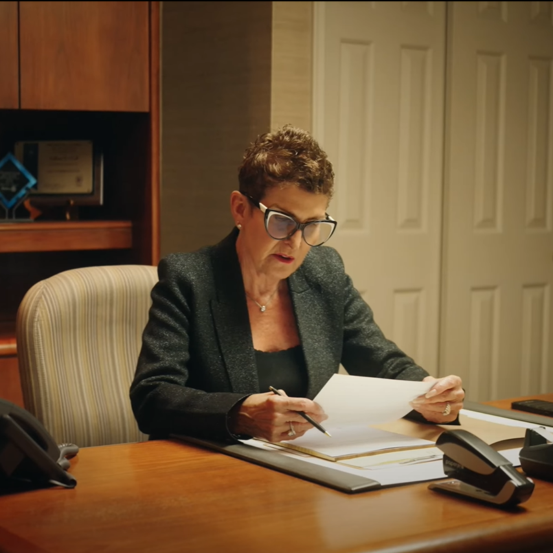 A female attorney sits at a wooden desk looking at case papers.