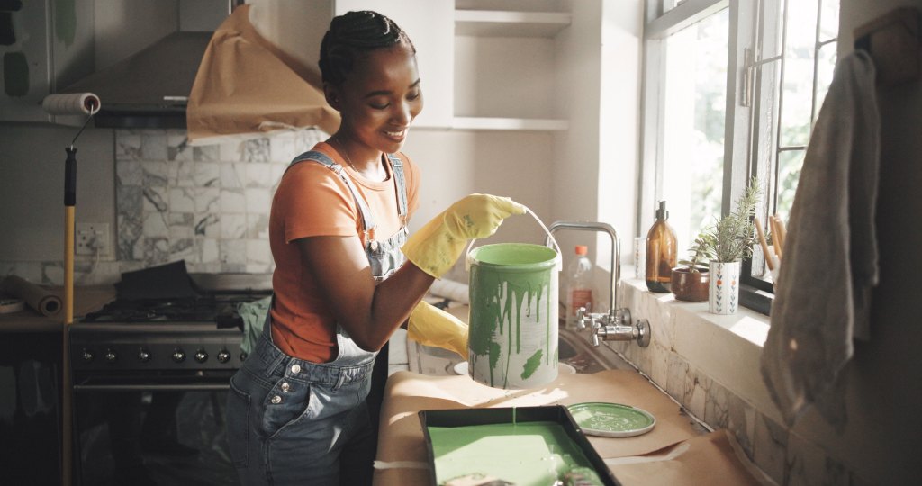 A woman stands in the kitchen, pouring green paint into a paint tray.