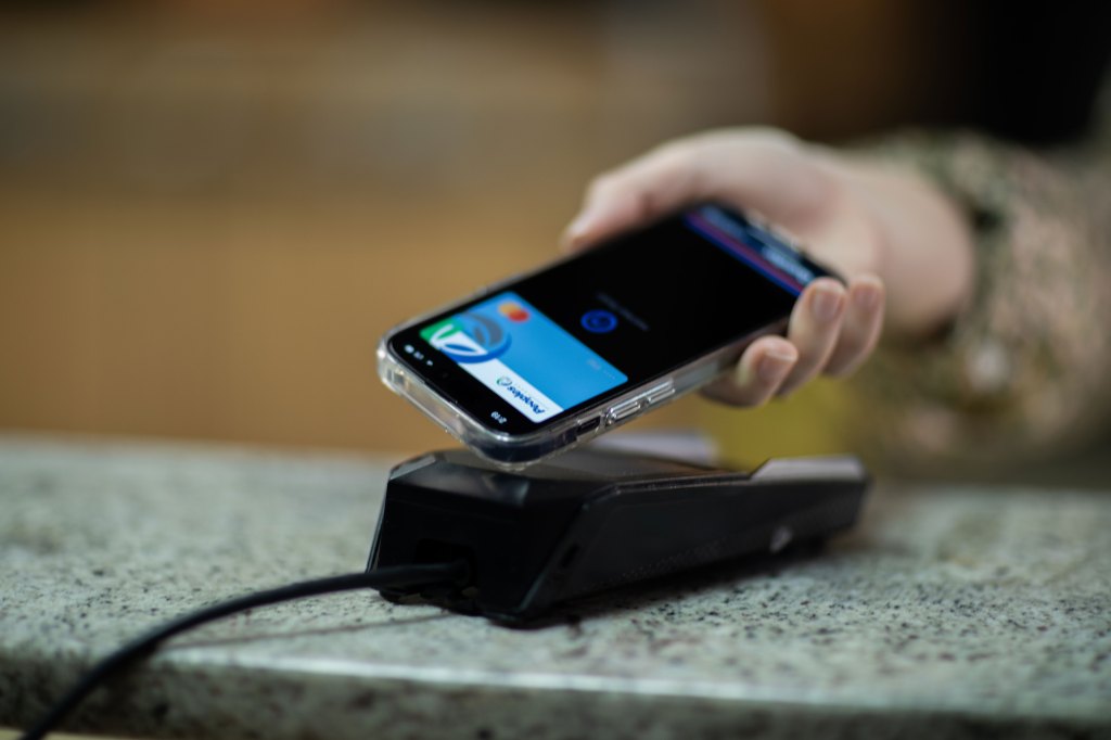 A person uses the mobile wallet function on their phone to make a transaction on a desk kiosk.