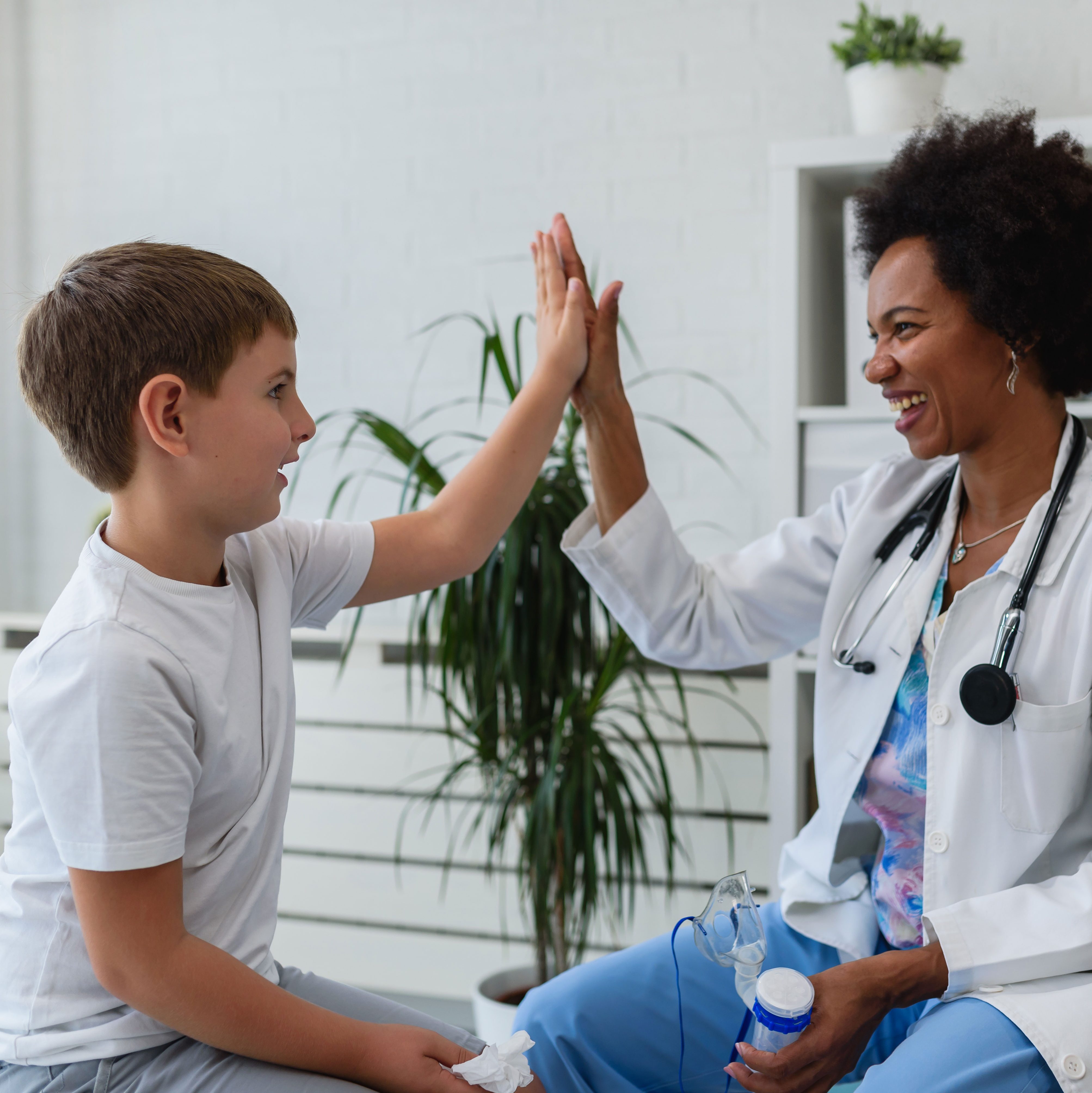Smiling female doctor gives a child a high five before a medical examination.