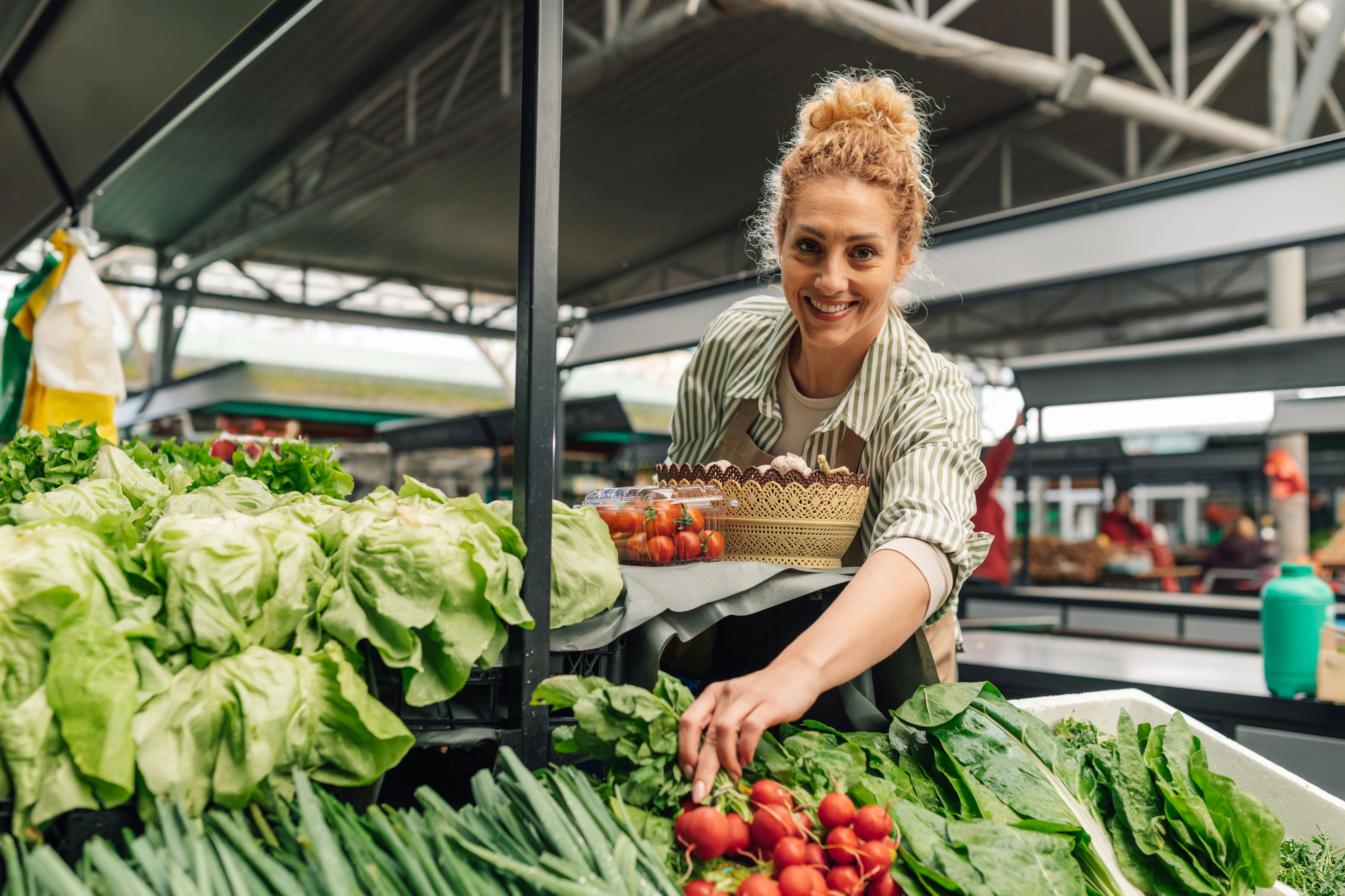 Smiling female farmer standing at an outdoor market and selling produce.