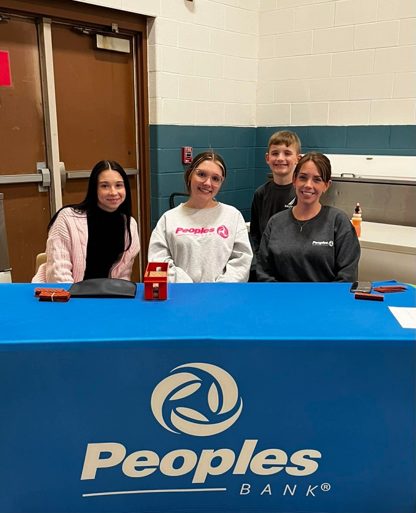 Three Peoples Bank associates sit at a table at Spencer Elementary School for a quarter auction event.