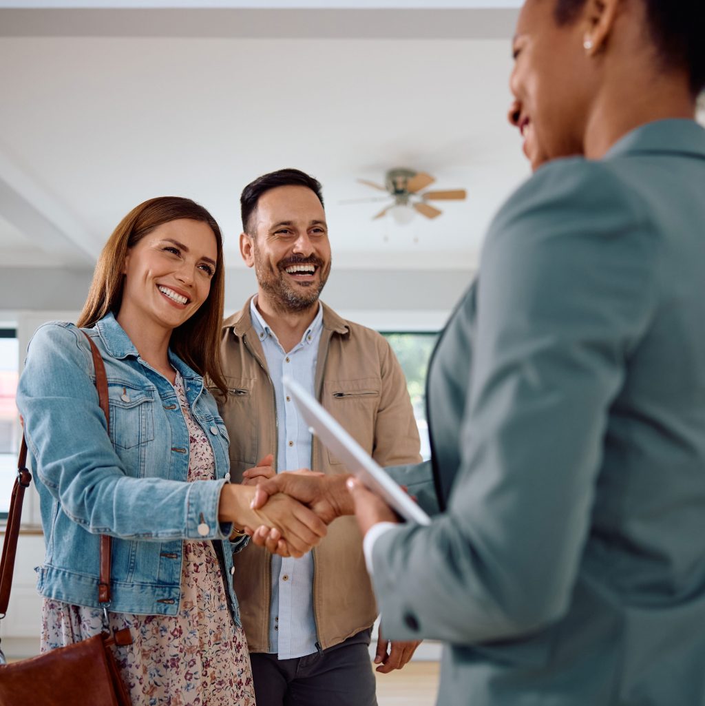 Woman shaking hands with real estate agent while buying a new apartment with her husband.