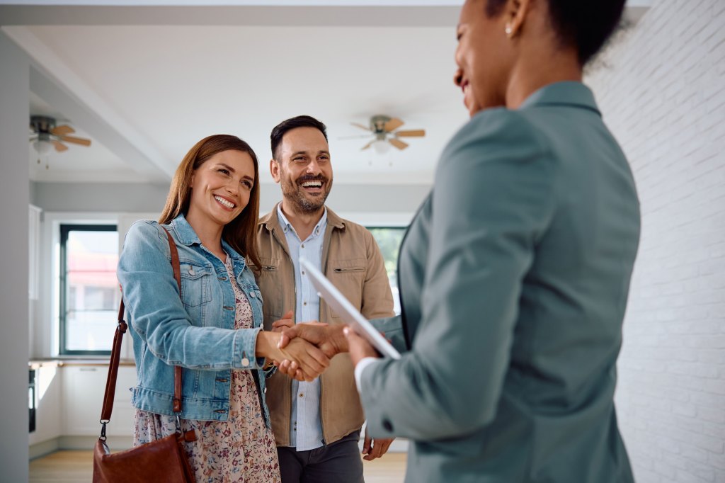 Woman shaking hands with real estate agent while buying a new apartment with her husband.