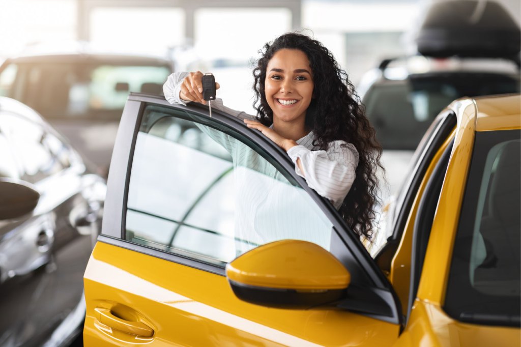 A young woman holding keys, buys a new car while standing in a showroom interior.