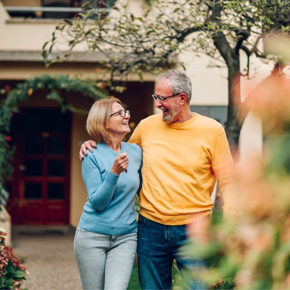 Senior female holding keys (left) and senior male (right) stand outside their new home.