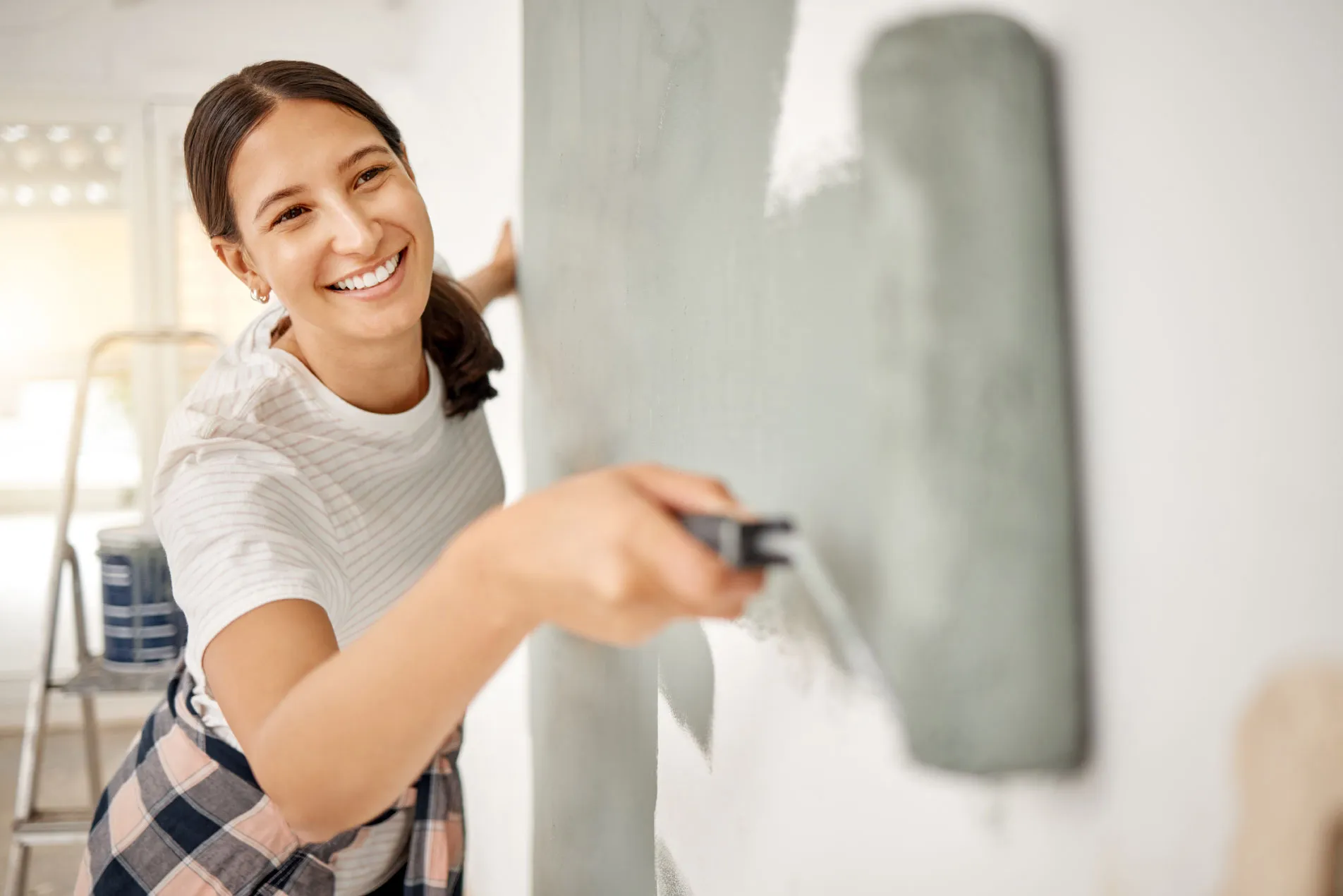 A woman paints a wall in her home gray using a handheld roller brush.