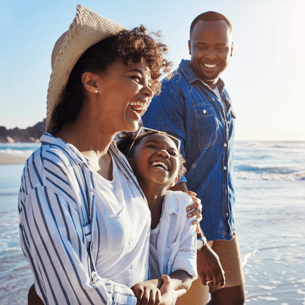 Parents and their daughter smile as they walk along the beach.
