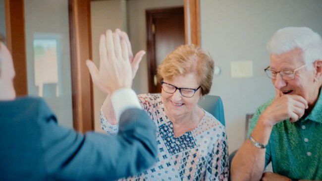 A senior woman and man sit at a conference room tablet with a Peoples Bank financial advisor. The woman high fives the financial advisor.