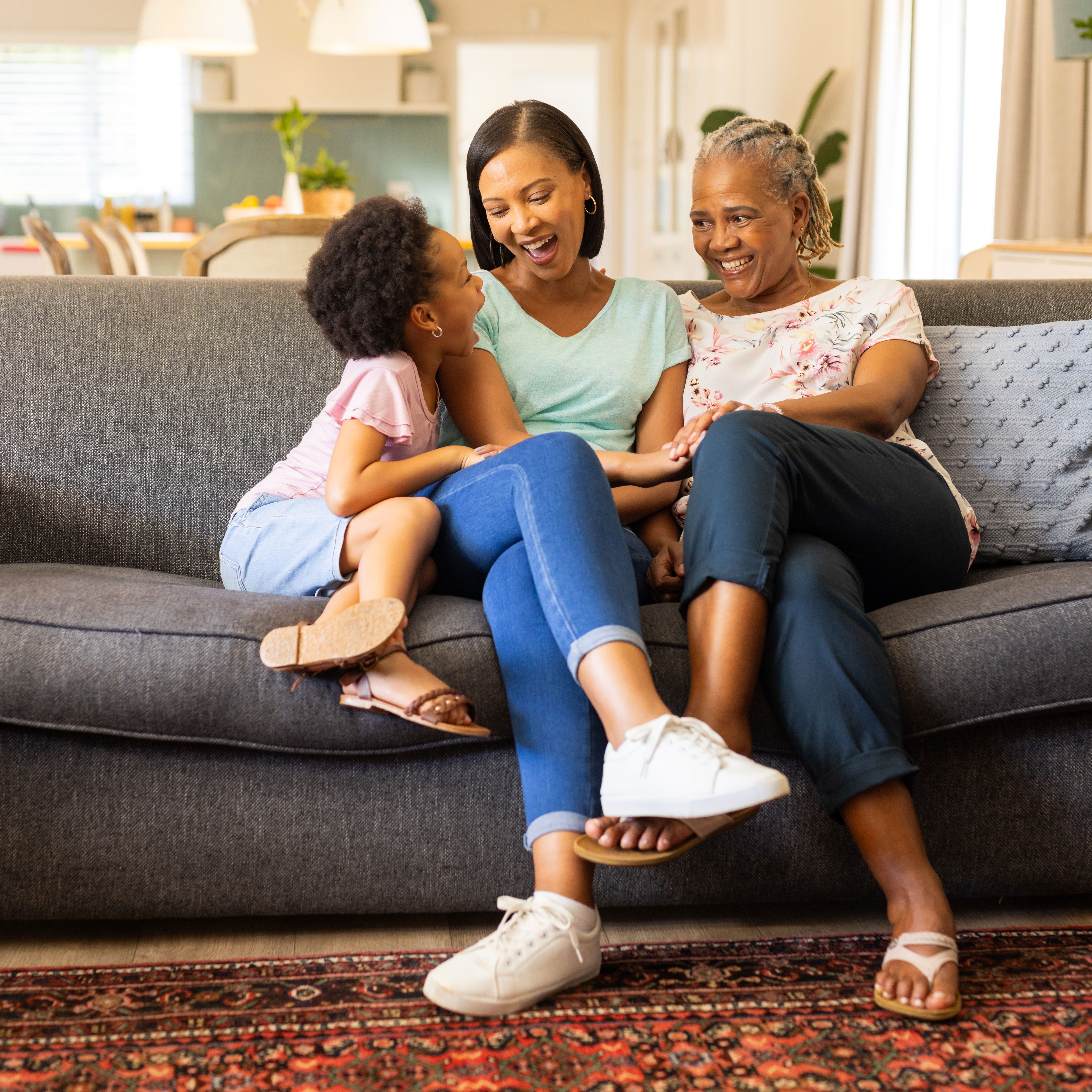 A young child, her mother, and grandmother sitting on a couch laughing.