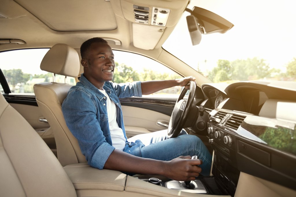 A happy young man driving a car (inside shot of car interior).