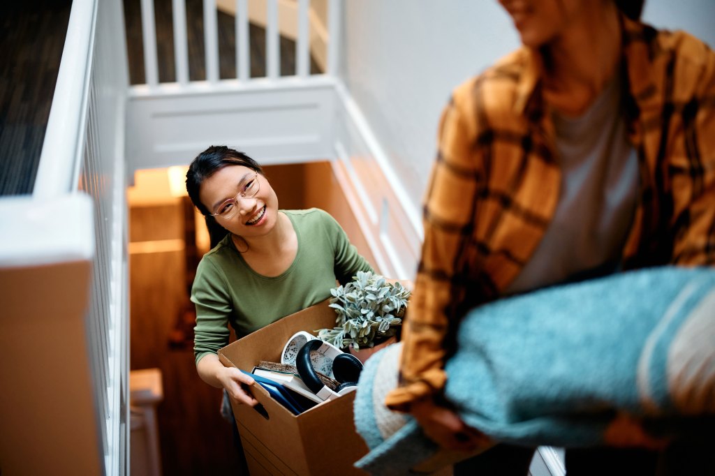 A happy young woman walks up a stairwell behind her friend while moving into a new apartment.