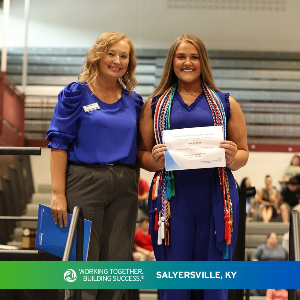 A high school student stands on a stage in Salyersville, Kentucky, while a Peoples Bank associate presents the Robert Evans Scholarship to them.